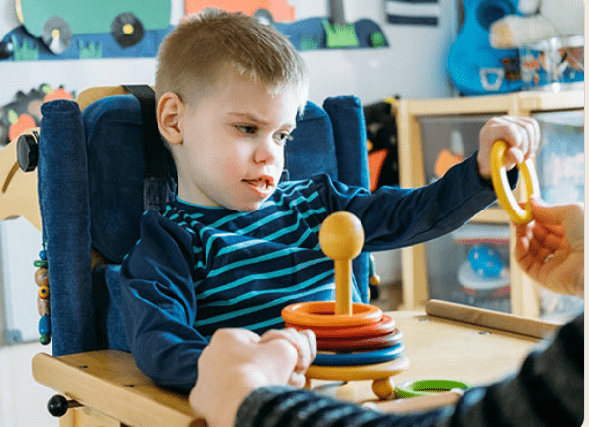 A child with cerebral palsy uses a walker while laughing in a playground.